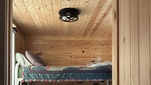 Un interior de madera con dos literas, una lámpara en el techo y una ventana.