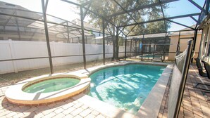 Une piscine avec un jacuzzi, entourée d’un patio couvert et d’une clôture blanche.
