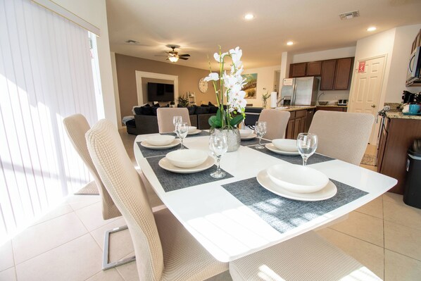 A dining area with a table set for four, including plates, glasses, and a vase with flowers. - Family Pool Home w/ Spa & Game Room (Davenport)