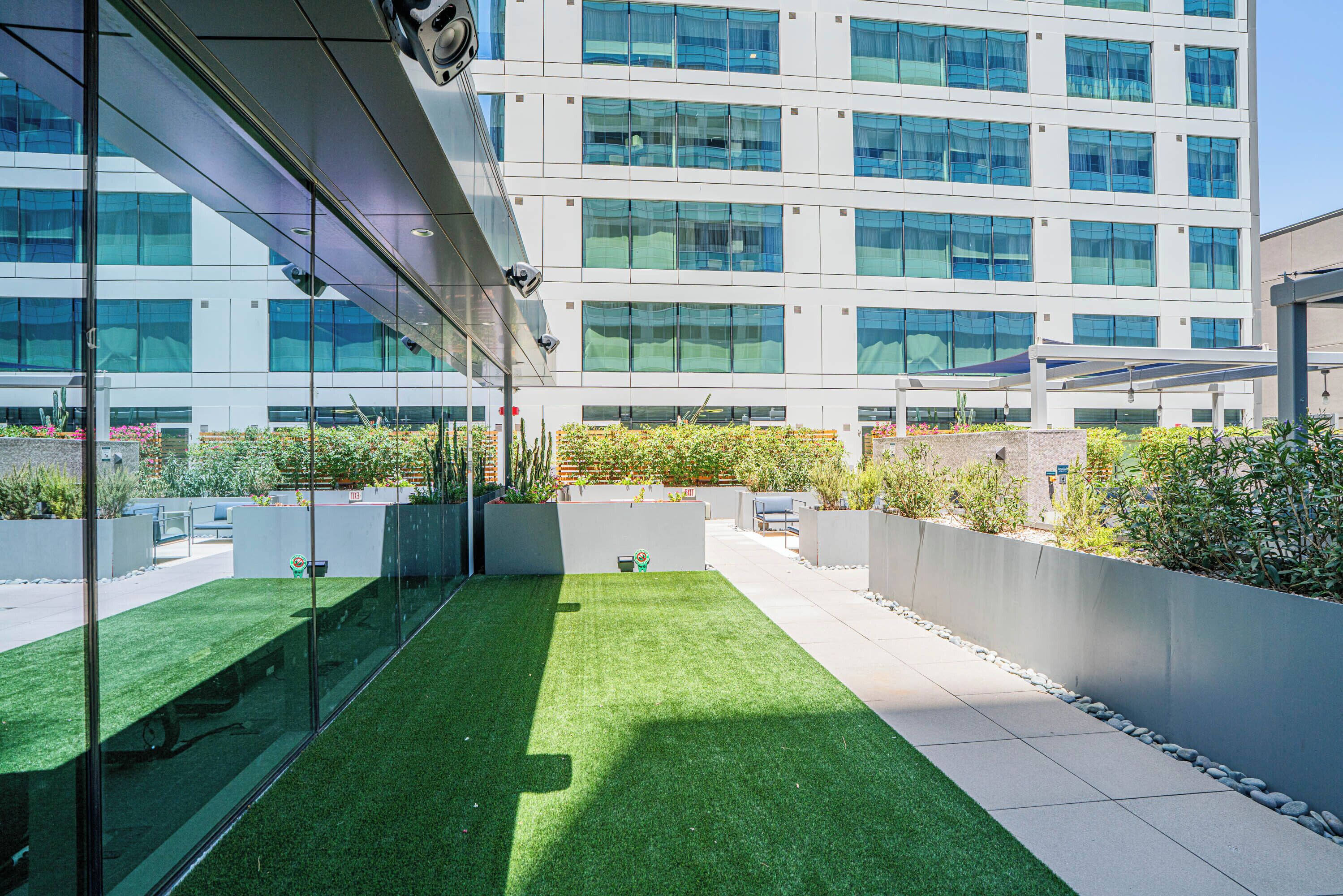 A modern building with a rooftop garden, glass walls, and a clear view of the sky.