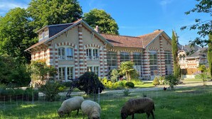 Un grand bâtiment historique à la façade symétrique, doté de nombreuses fenêtres et agrémenté d’un jardin bien entretenu où paissent des moutons.
