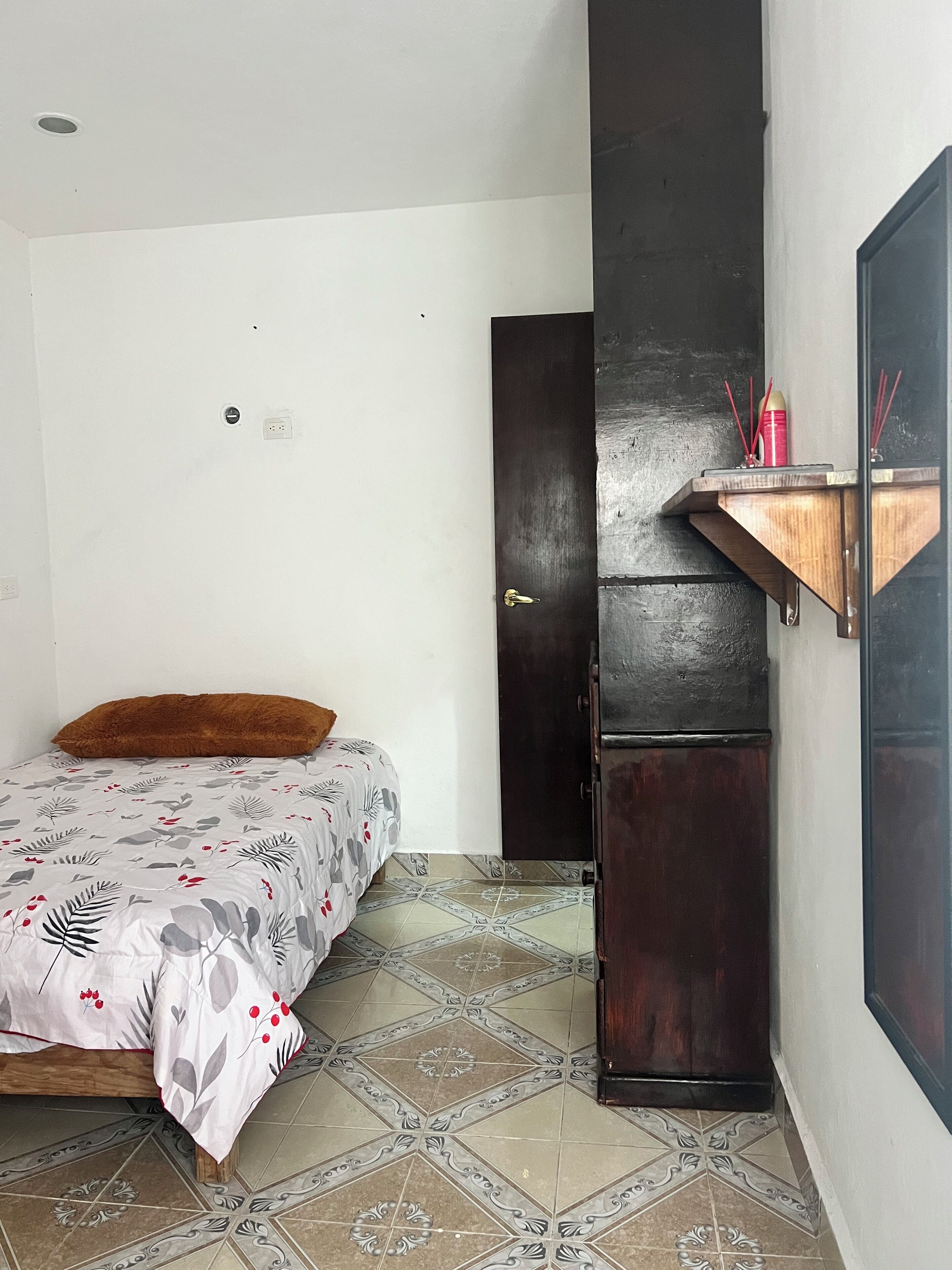 Un dormitorio con cama, armario de madera, estante con palitos de incienso y baldosas de suelo estampadas.