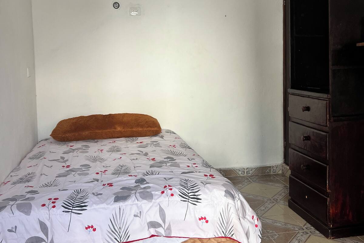 A bedroom with a bed, a wooden headboard, a wardrobe, and a tiled floor.