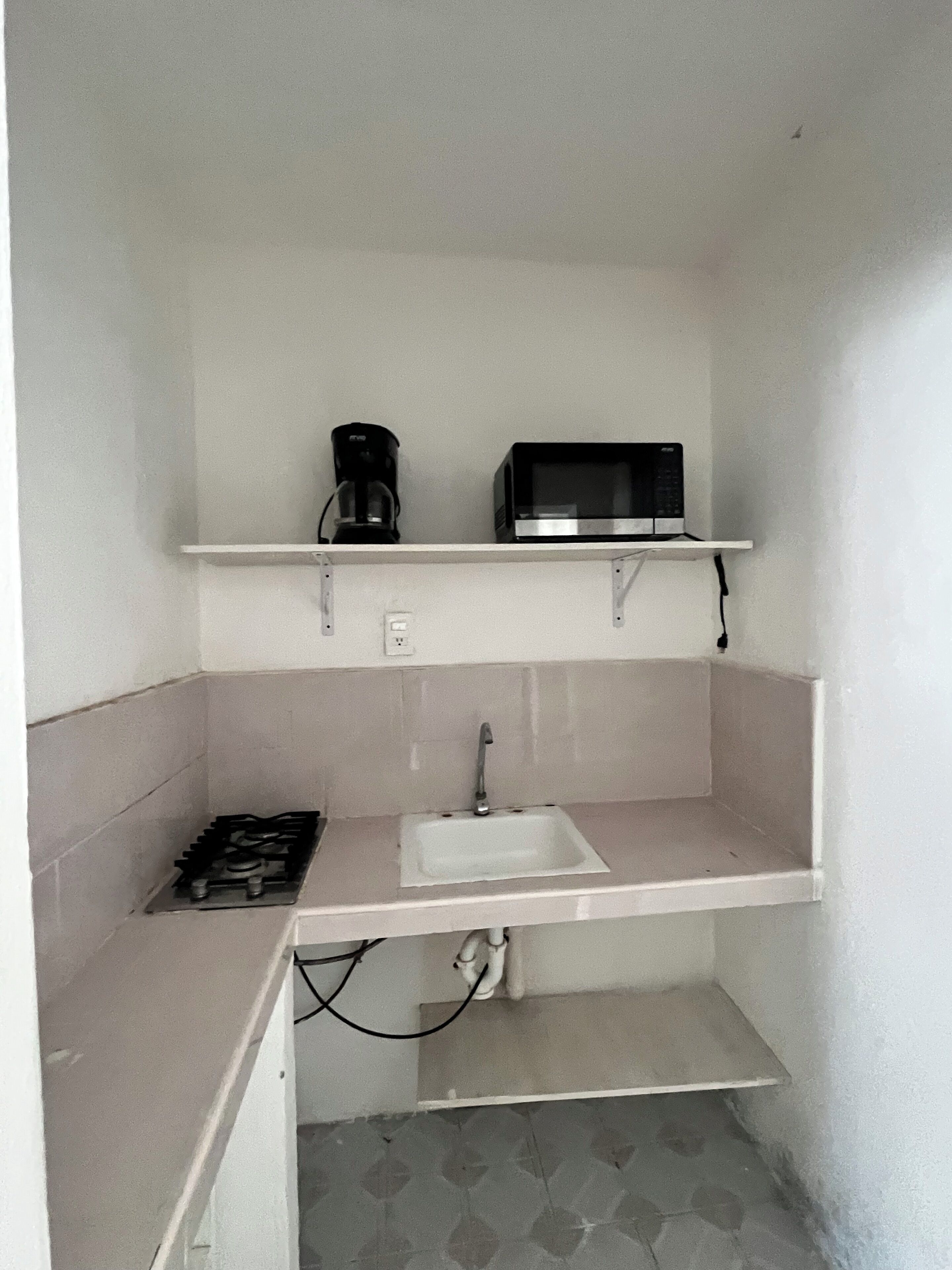 Una cocina compacta con estufa a gas, un lavamanos y un microondas sobre una repisa.