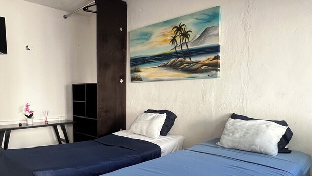 A room with two beds, a desk, and a painting of a beach scene. - HOSTAL MID GY (Mérida)