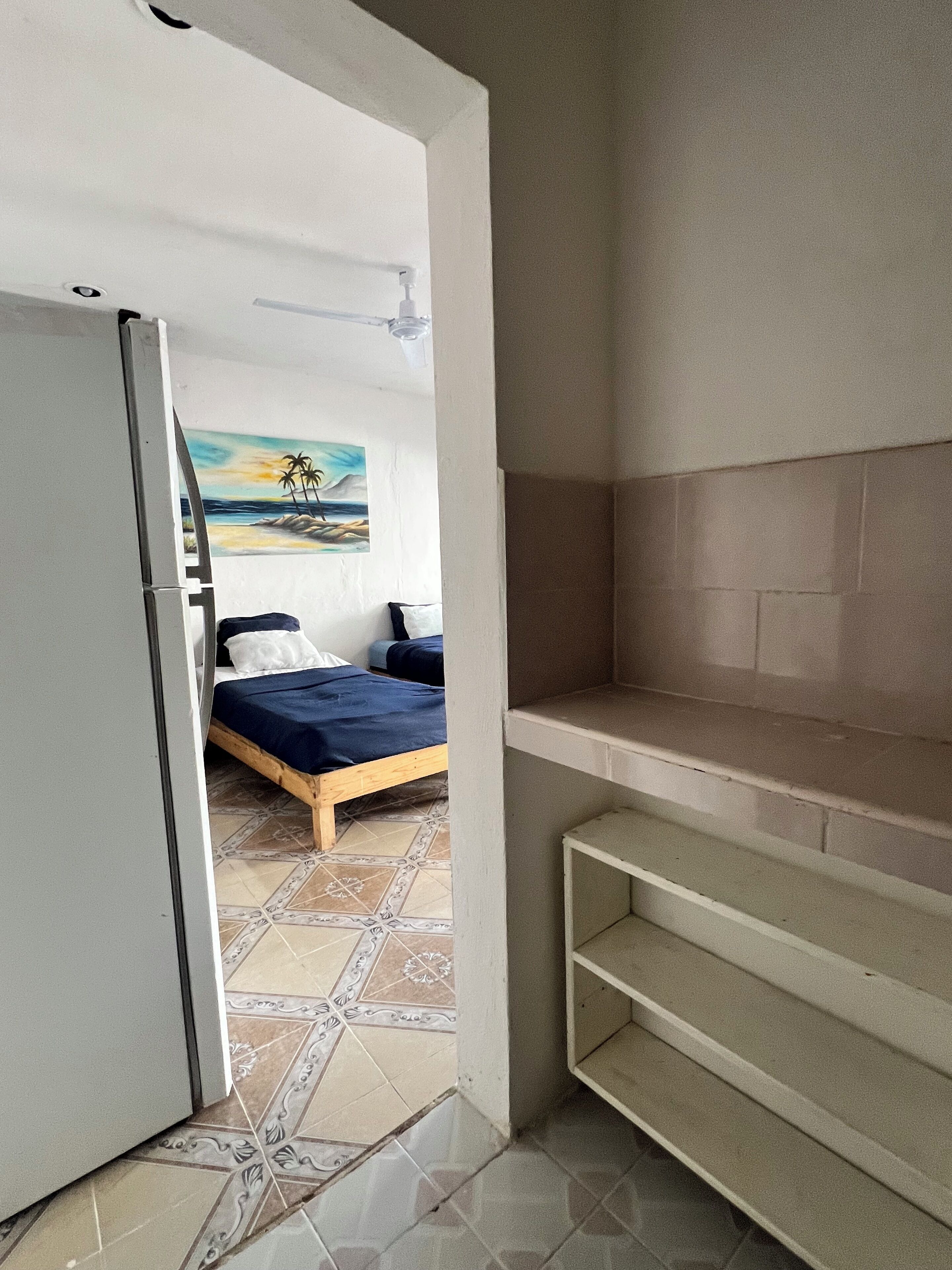 Un dormitorio con una cama, un cuadro, un armario blanco y suelo de baldosas.