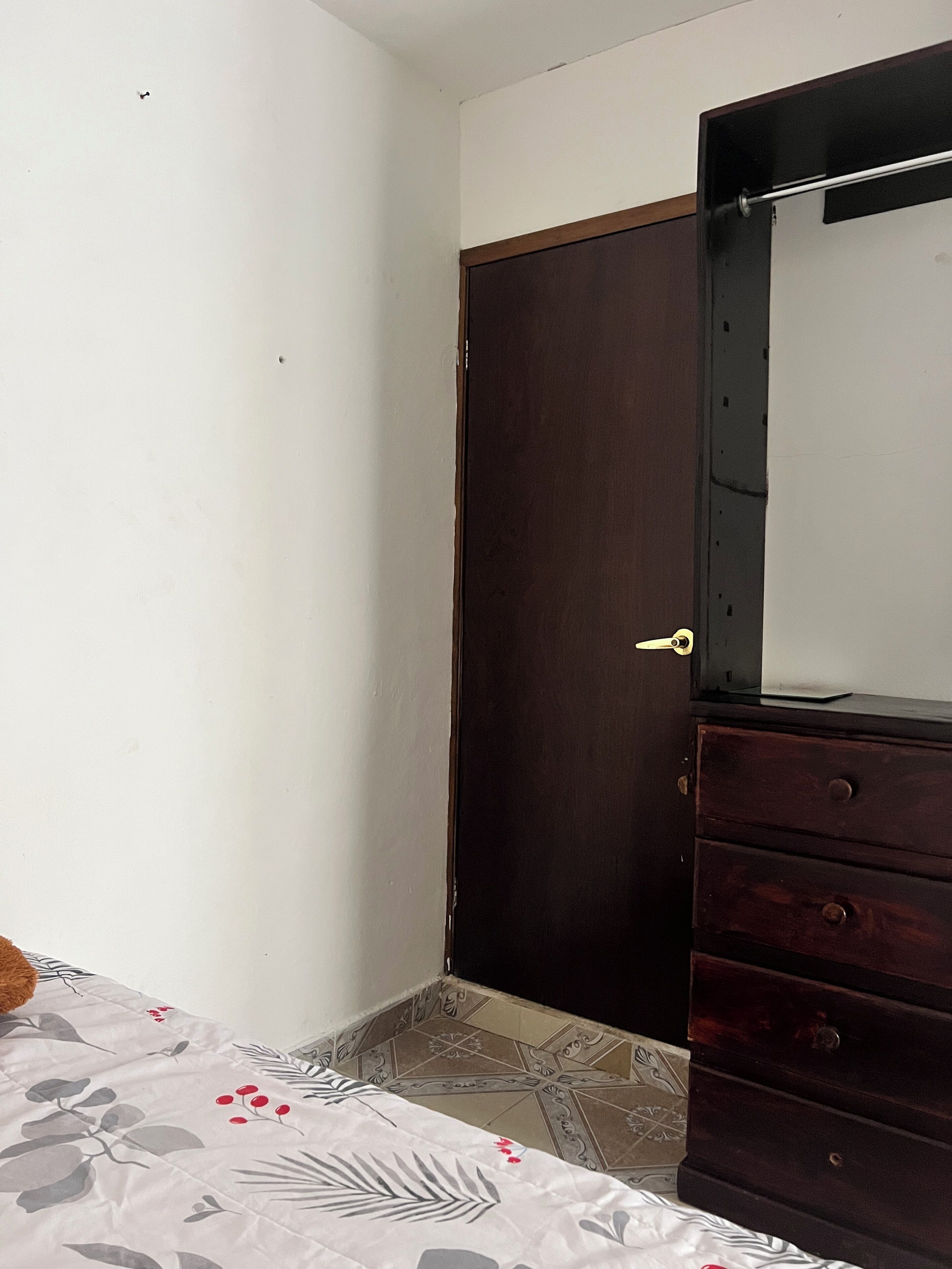 A bedroom with a bed, a dresser, a wardrobe, and a mirror.