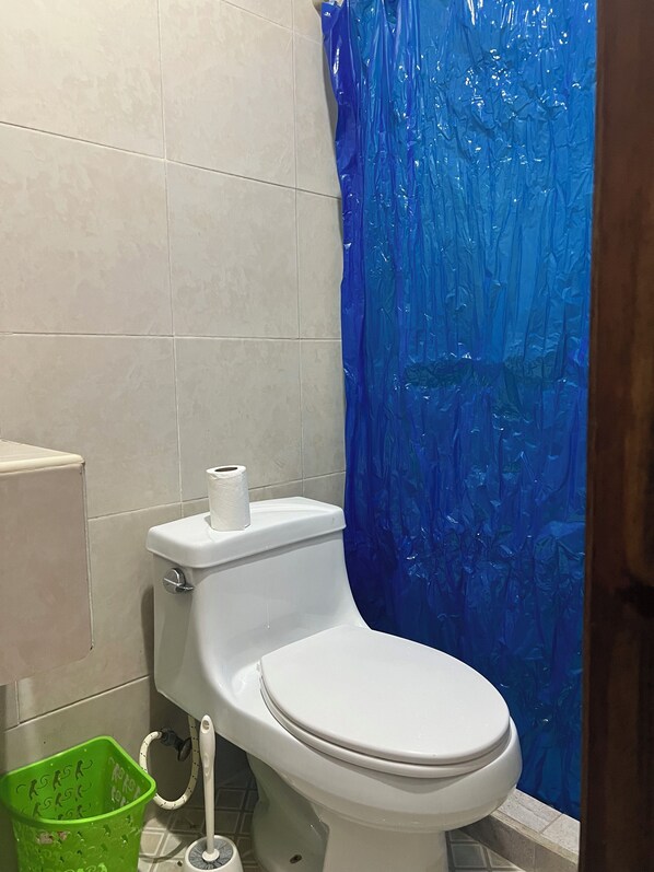 Casa de banho com sanita, um caixote de lixo verde e uma cortina de chuveiro azul.