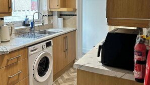 A compact kitchen with wooden cabinets, a built-in washing machine, a sink, and a window with a view of the outside. - Comfortable Stay with Free Parking (Moor Row)