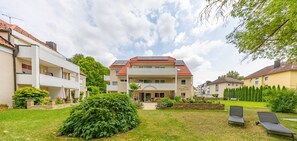A residential building with a red-tiled roof, multiple balconies, and a well-maintained garden with a lawn and a bench. - New apartments in a very quiet location in the city center—accessible to people with limited mobility (Bad Wörishofen)