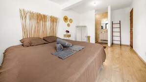 A bedroom with a large bed, a wooden ladder, and a bathroom visible through an open door. - Villa Rêve Austral (Saint-Pierre)