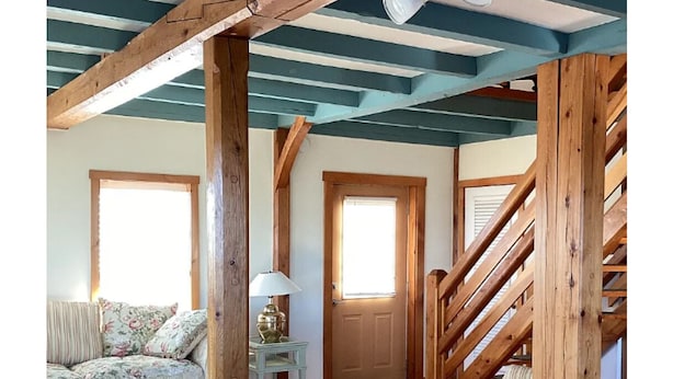 Une pièce avec des poutres en bois, un escalier, un canapé, une lampe et un tapis.