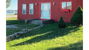 Un bâtiment en briques rouges, avec une porte blanche, deux fenêtres et un toit rouge.