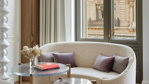 Una habitación con sofá, una mesa de vidrio y vistas a un edificio a través de una ventana.