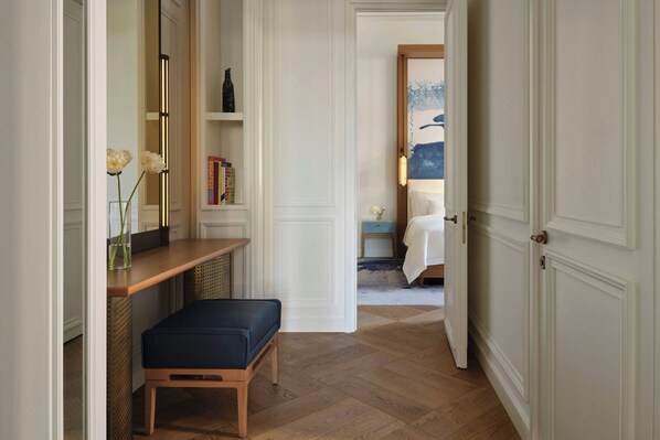 A hallway with a bench, a mirror, a vase with flowers, a bookshelf, and a door leading to another room. - The St. Regis Budapest (Budapest)
