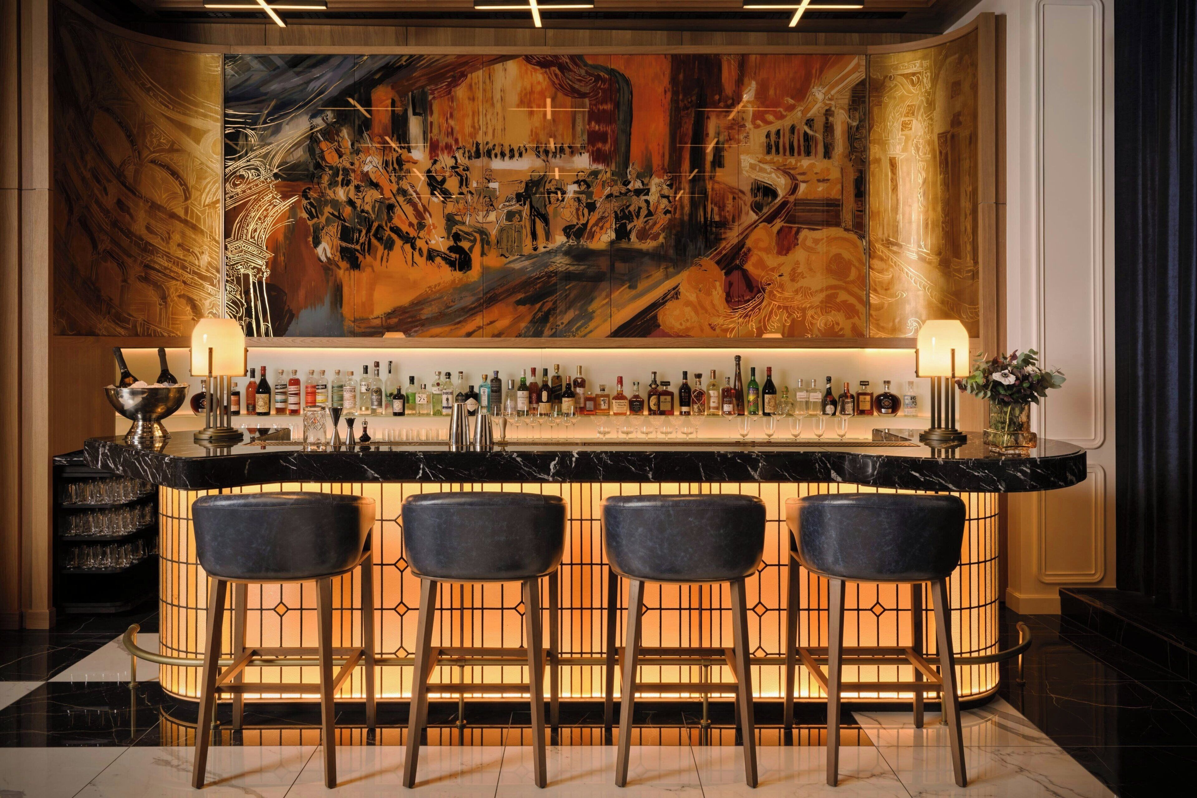 A bar area with a marble countertop, three black bar stools, and a large abstract painting on the wall.