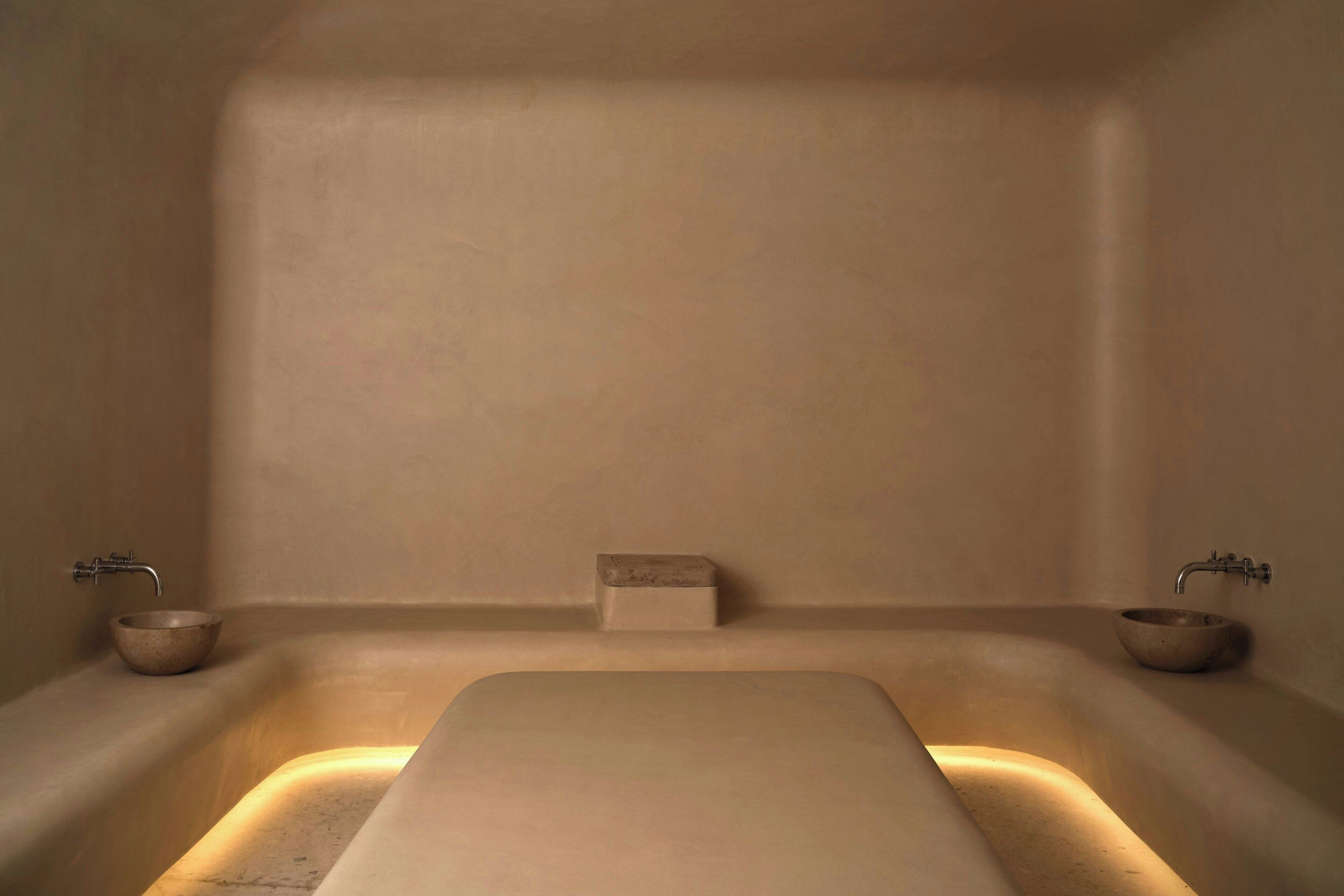 A minimalist bathroom with a central bathtub, two side basins, and a small rectangular object on the wall.