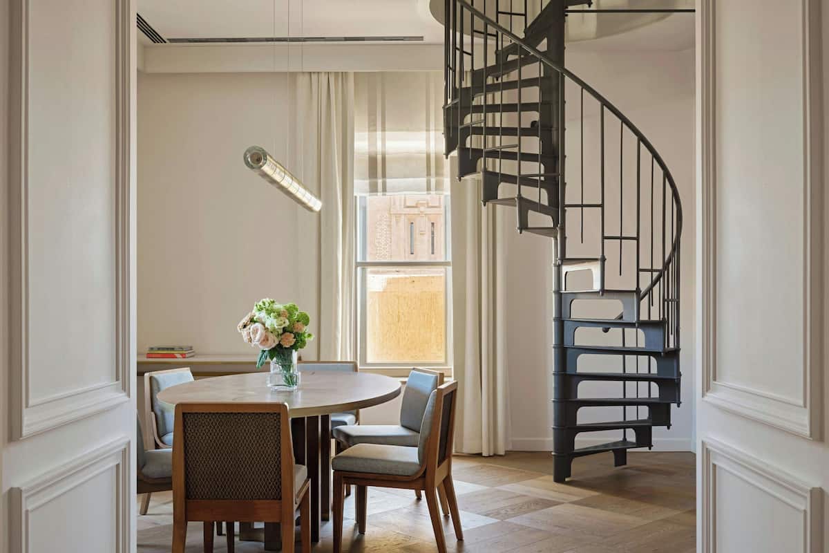 Un comedor con una mesa redonda, sillas, un florero con flores y una escalera en espiral negra.