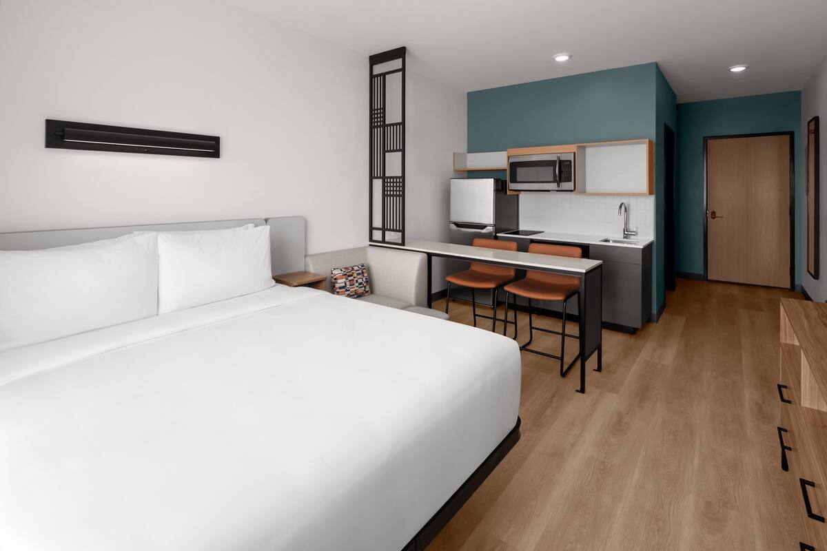 A hotel room with a bed, a desk with two chairs, a microwave, and a sink.