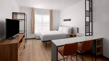 A modern hotel room with a bed, desk, chairs, a TV, and a window with curtains.