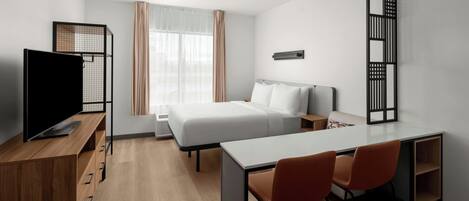 A modern hotel room with a bed, a desk, two chairs, a TV, and a window with curtains.