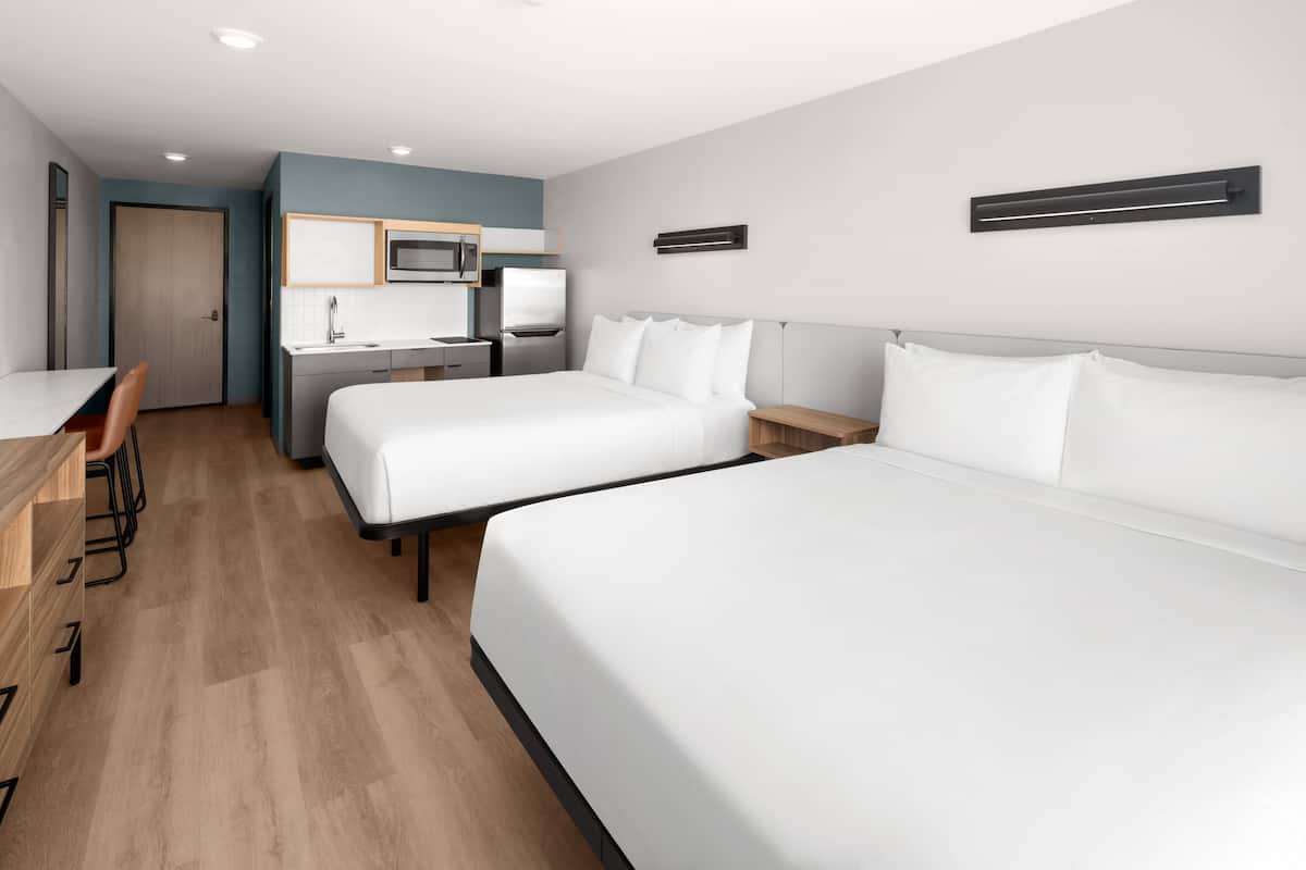 A hotel room with two beds, a kitchenette, a desk, and a chair.