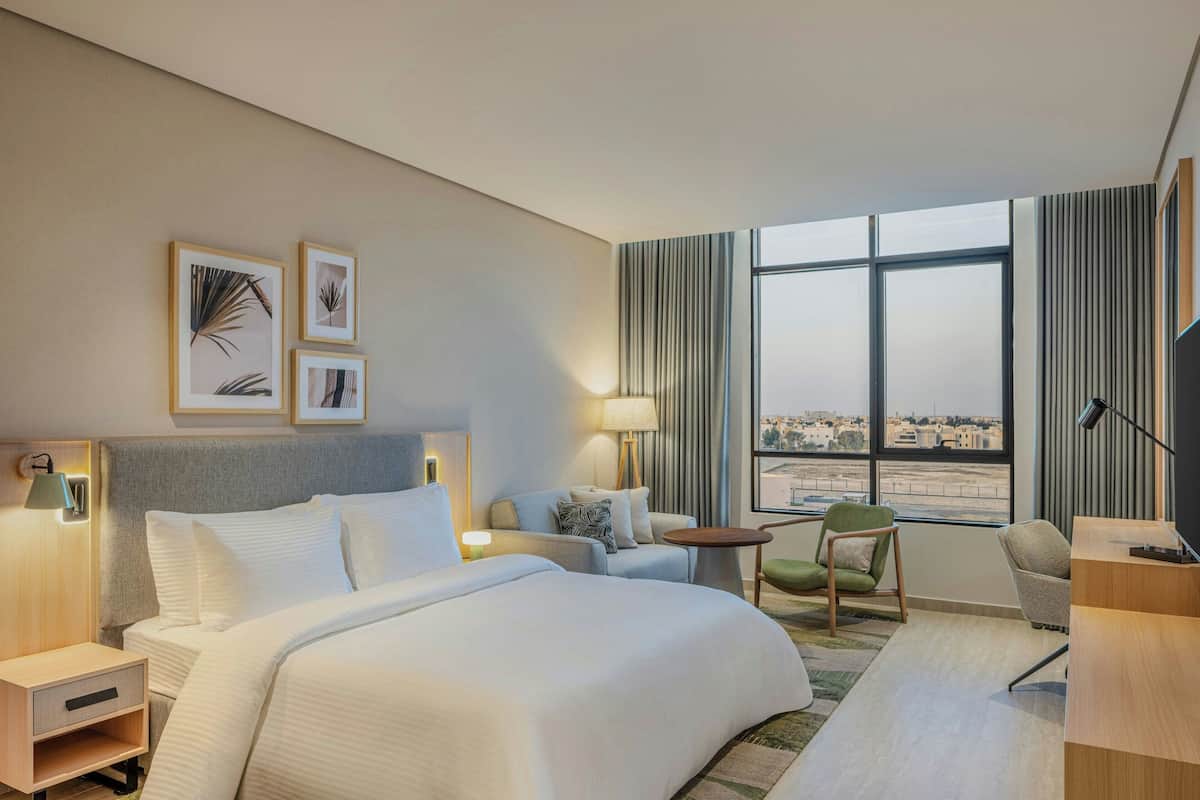 Habitación de hotel con una cama grande, un escritorio, una silla, un televisor y una ventana con vista a la ciudad.