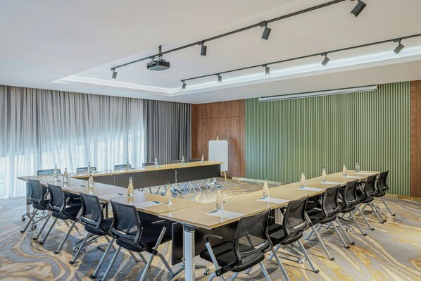 Un salón de conferencias con una larga mesa, sillas, un atril y un proyector.