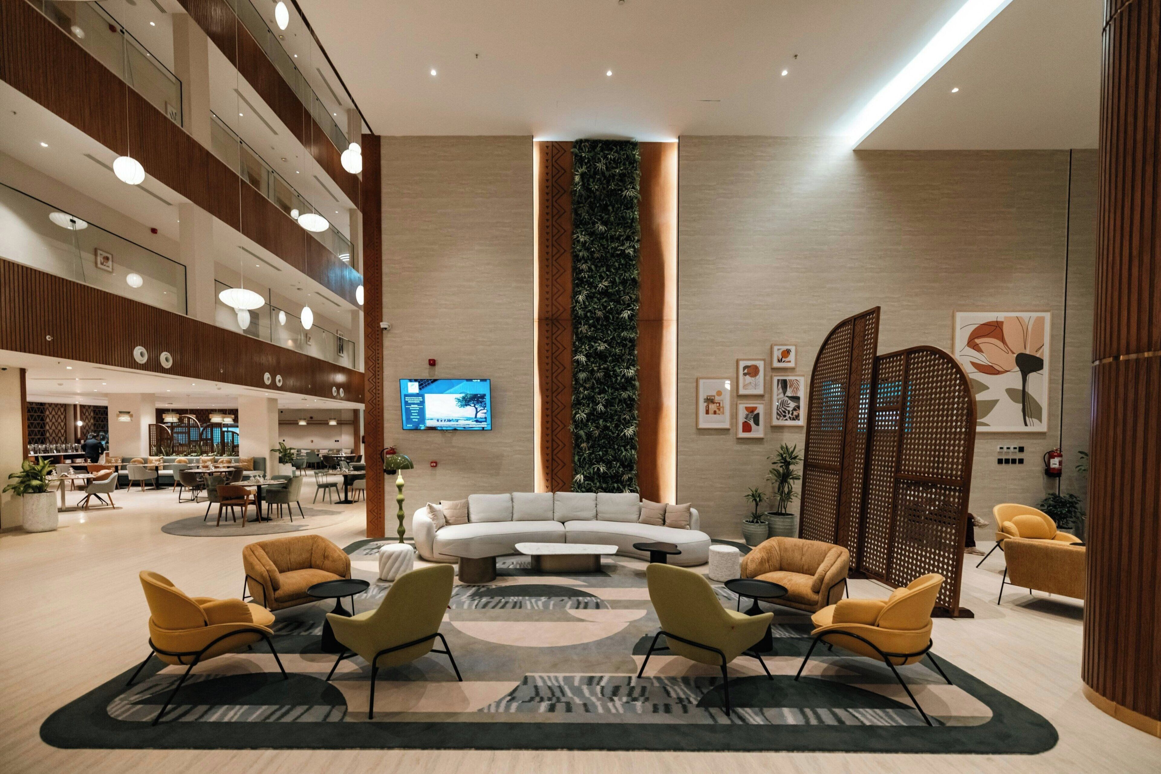 Um lobby de hotel moderno com uma área de estar central, uma grande tela de televisão e um jardim vertical.
