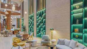 Eine moderne Lobby mit einer gebogenen Couch, runden Tischen und grünen Regalelementen.