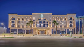 Ein mehrstöckiges Hotel mit einem markanten Eingang, Palmen und einer gut beleuchteten Fassade.