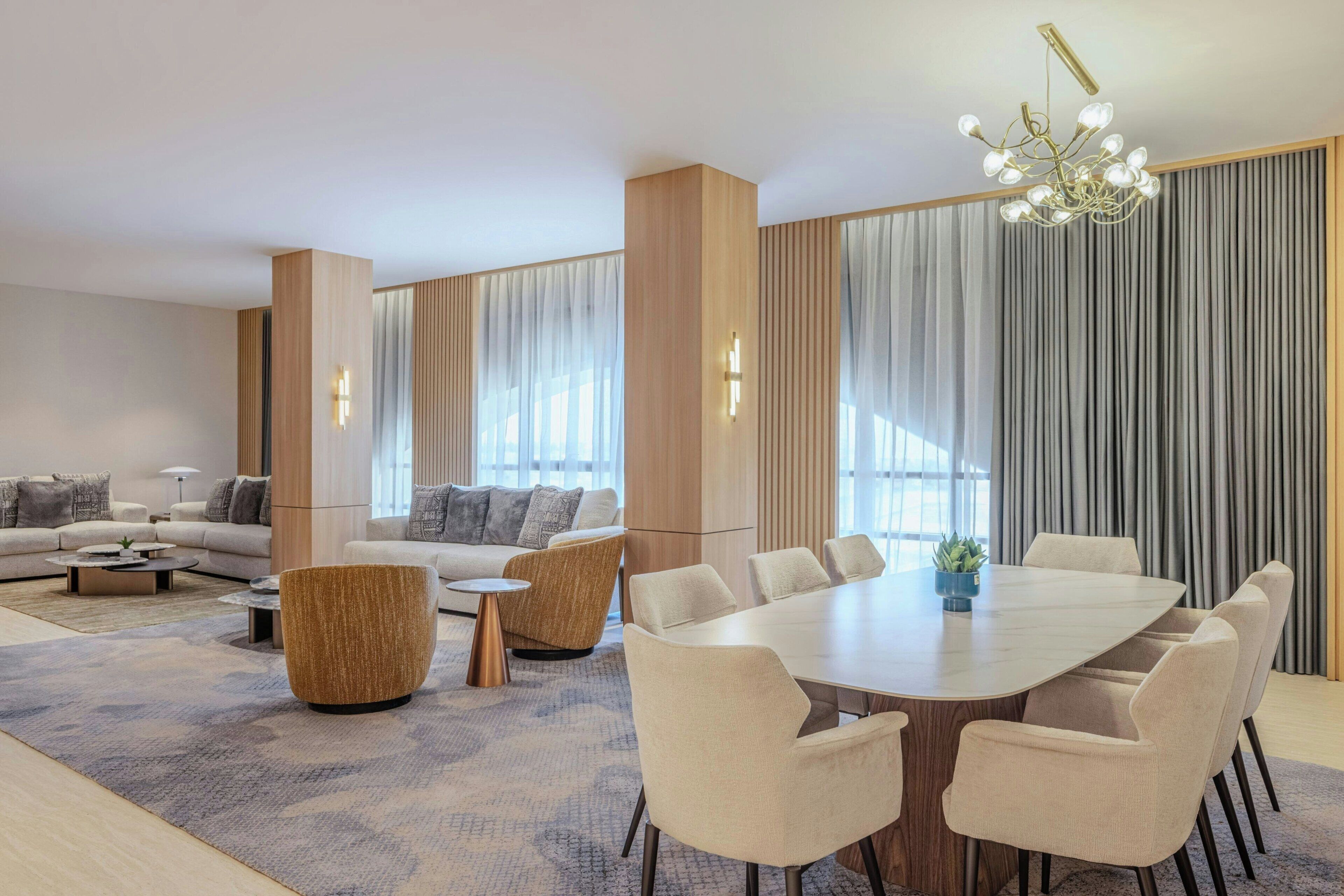 A modern living room with a large dining table, sofas, and a chandelier.