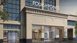 Ein modernes Gebäude mit der Beschilderung "FOUR POINTS BY SHERATON", das ein Hotel kennzeichnet. Es verfügt über große Fenster, einen Glasvordereingang und eine Stein-Fassade.