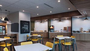 A modern restaurant interior with multiple dining tables and chairs, a kitchen area, and a chalkboard with motivational writing. - Fairfield By Marriott Inn & Suites York (York)