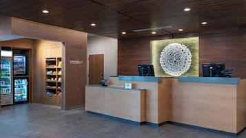 Een hotel receptie met een houten balie, een automaat en een decoratief object aan de muur.