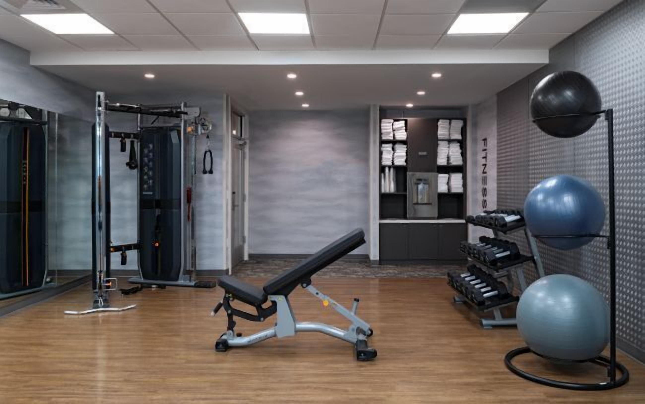 Un gimnasio con equipo de ejercicio, una banca y una pelota de ejercicio fijada a la pared.