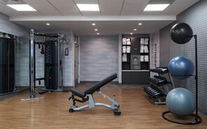 Ein Fitnessraum mit Trainingsgeräten, einer Bank und einem an der Wand befestigten Übungsball.