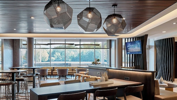 Un restaurante moderno con una larga mesa compartida, diversas opciones de asientos y un amplio ventanal con vistas al exterior.