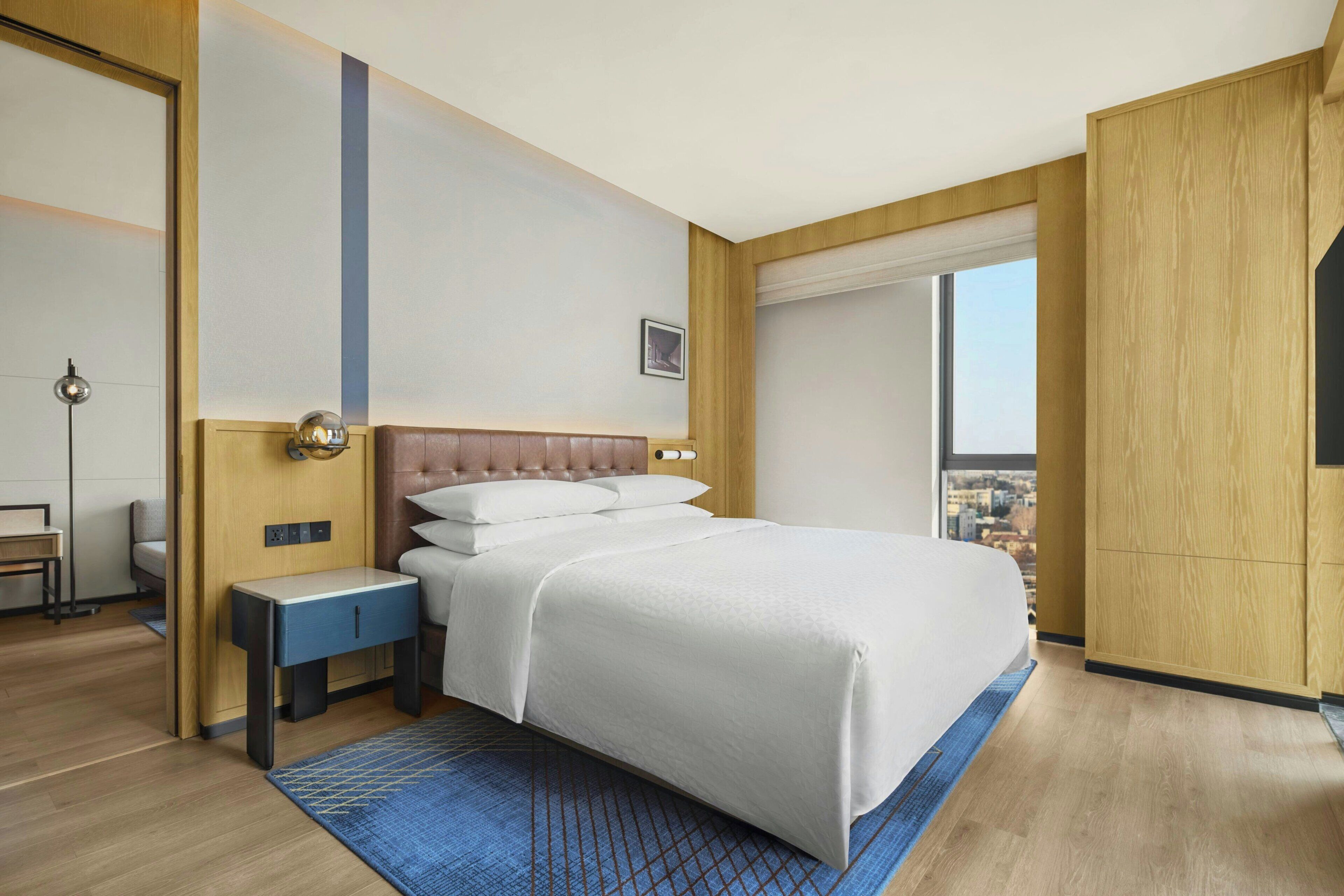 Habitación de hotel con una cama grande, una mesita de noche, un escritorio, una silla, una ventana con vistas a la ciudad y un armario.