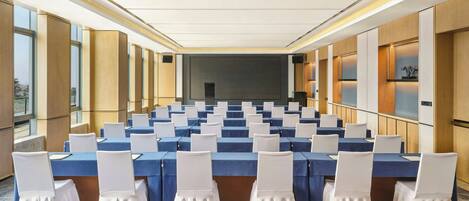 Un salón de conferencias con filas de mesas y sillas, ventanas amplias y un diseño interior moderno.