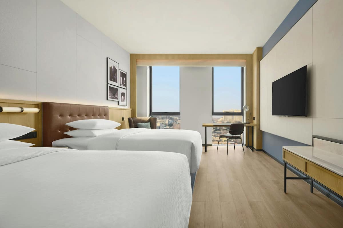 Ett hotellrum med två sängar, ett skrivbord, en stol, en TV och utsikt över staden.