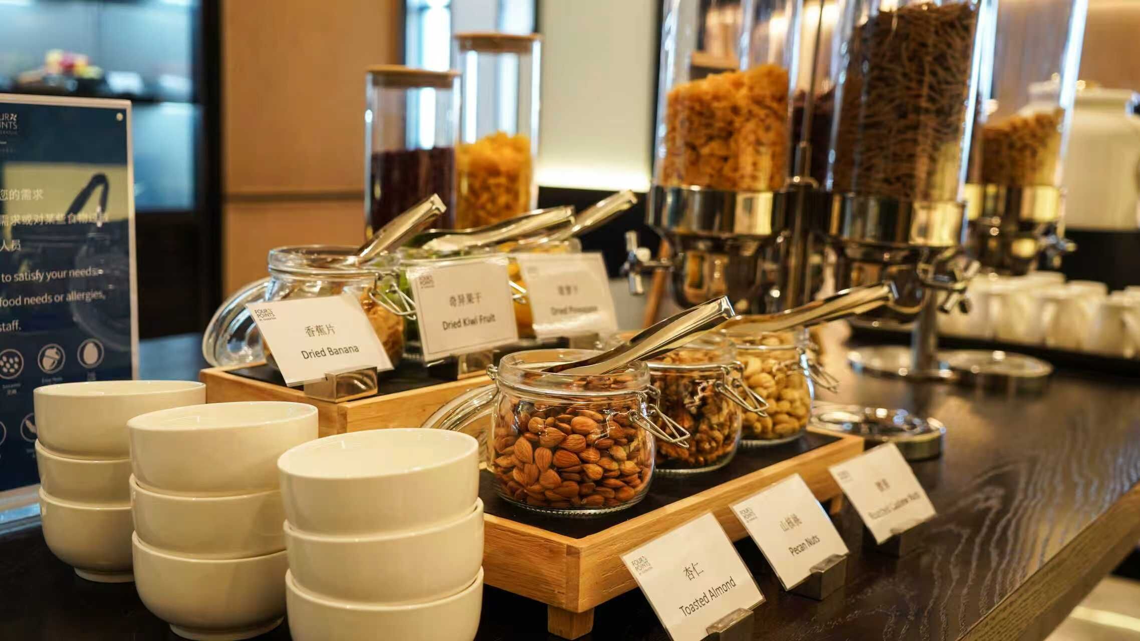Un bufé con alimentos etiquetados, incluyendo plátano deshidratado, kiwi deshidratado, almendras y nueces de pacana.