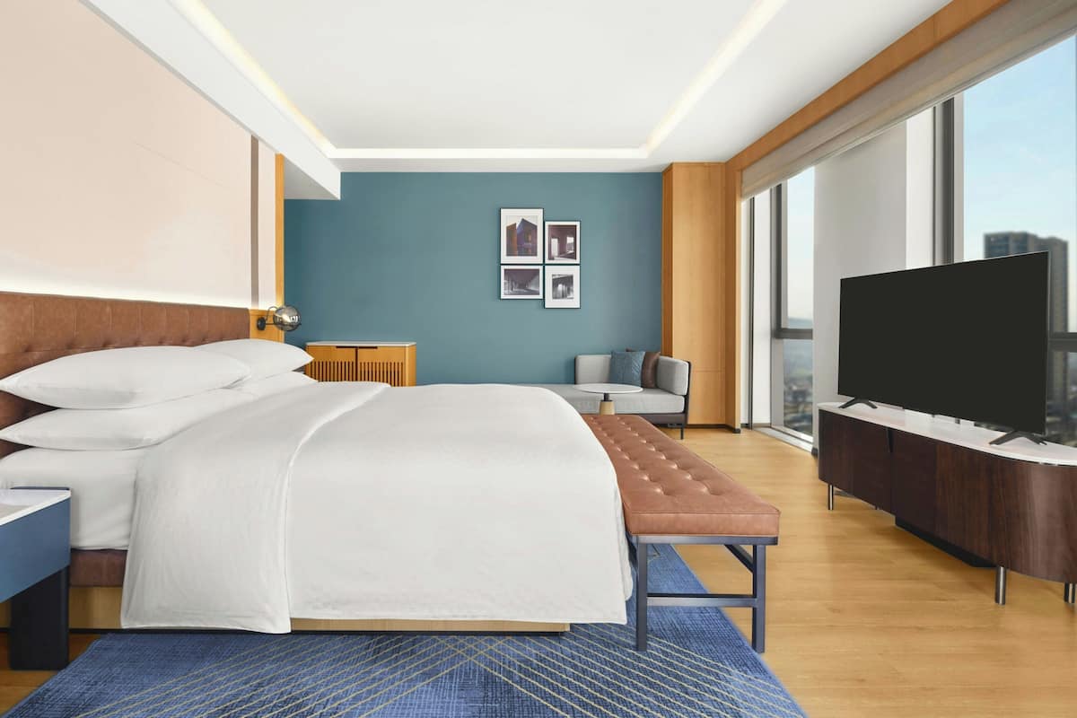 Ett hotellrum med en säng, en TV, en sittgrupp och ett stort fönster.