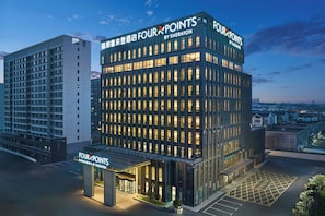 Un hotel moderno con fachada de vidrio, varios pisos y señalización destacada de 'Four Points by Sheraton'.