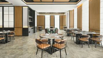 Un comedor de hotel espacioso con varias mesas y sillas, un diseño de techo moderno y grandes ventanales.