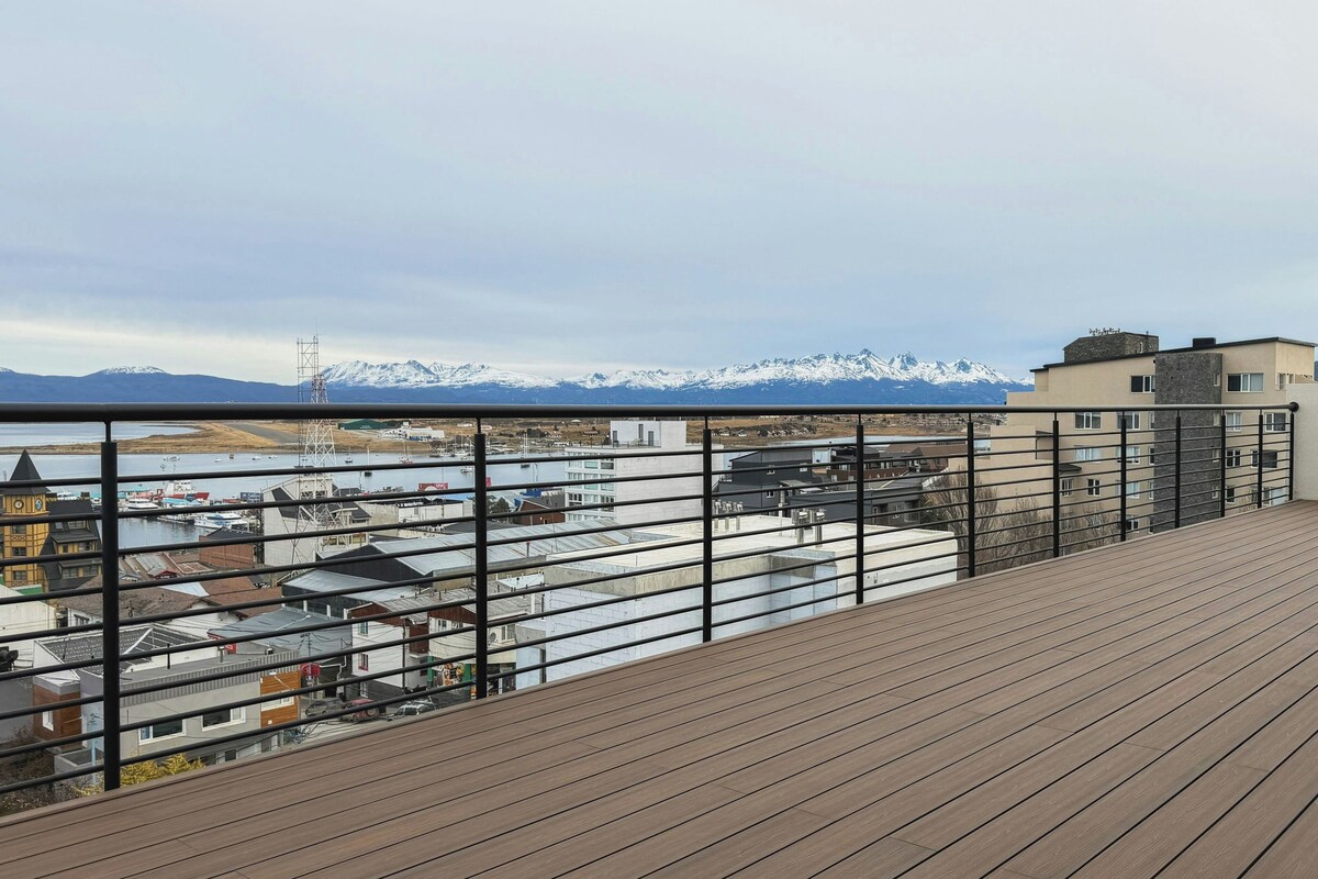 En träveranda med utsikt över en stad och snöklädda berg i fjärran.