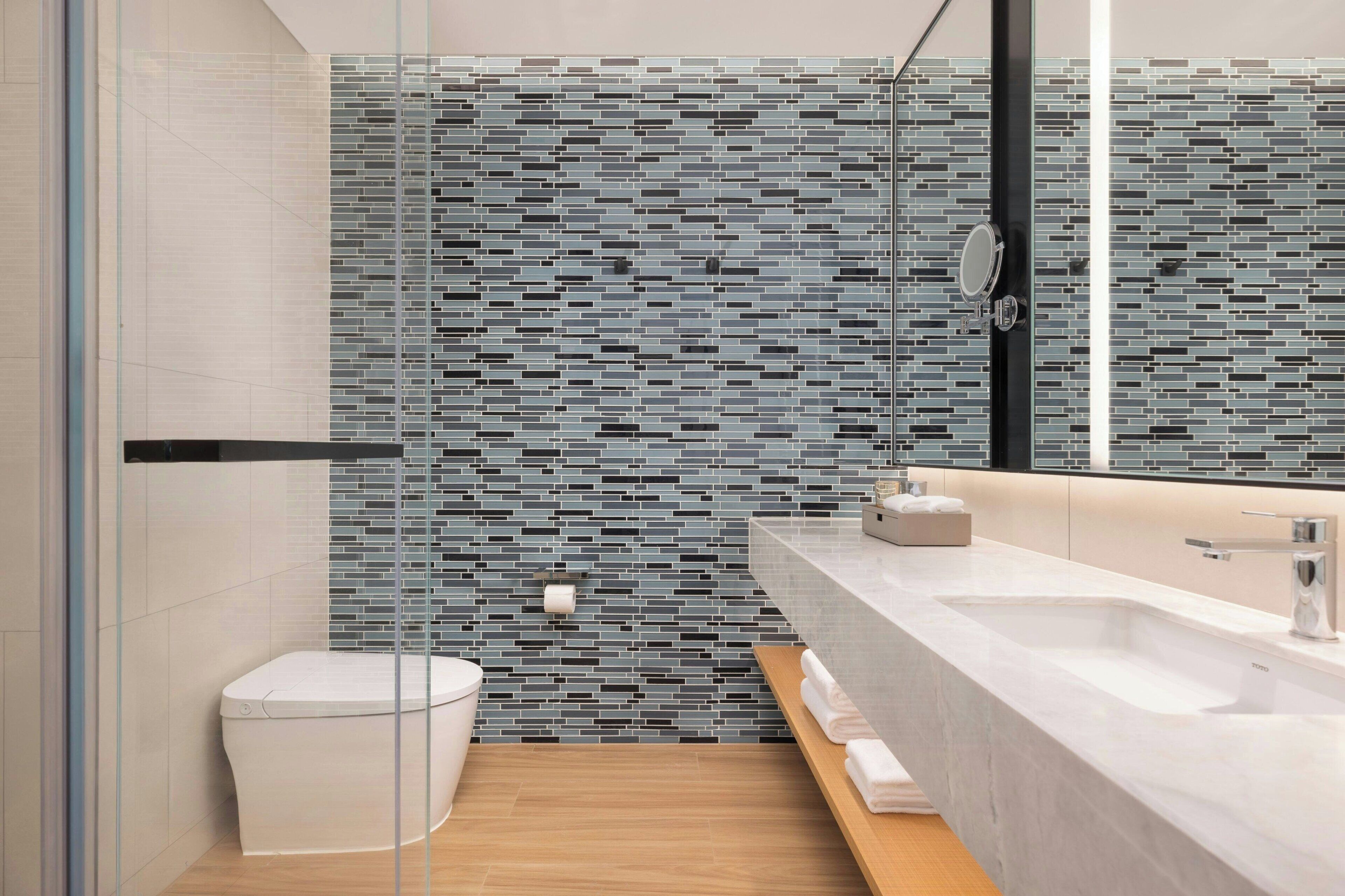 A modern bathroom with a glass shower enclosure, a white toilet, a sink with a mirror, and a tiled backsplash.