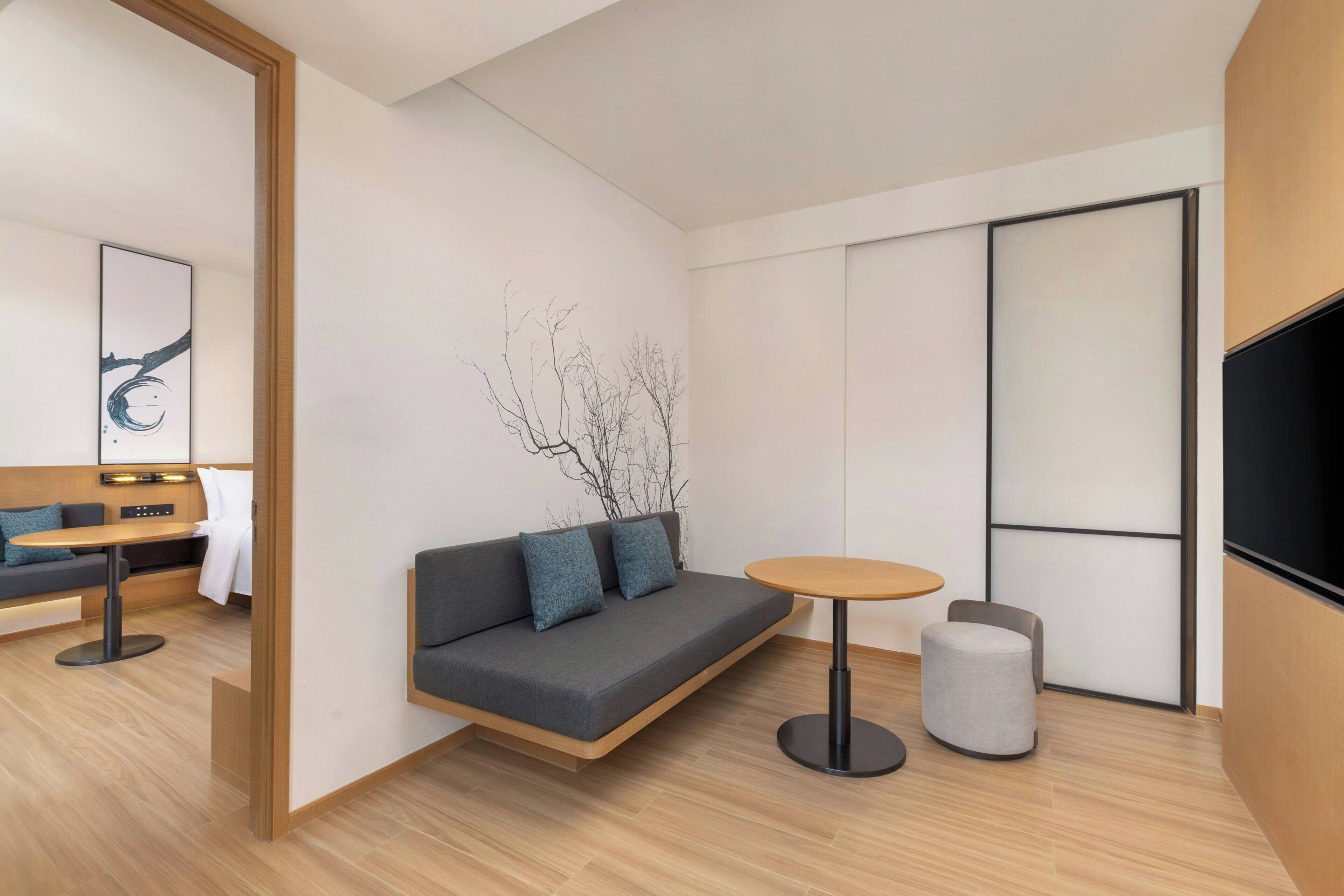 Una habitación moderna con sofá, una mesa redonda, un taburete pequeño, televisión y una obra de arte en la pared.