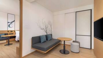 Una habitación moderna con sofá, una mesa redonda, un taburete pequeño, televisión y una obra de arte en la pared.
