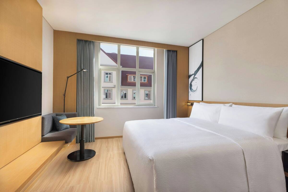 Habitación de hotel con cama, una mesita, un sofá, un televisor y una ventana con cortinas.